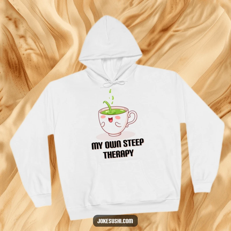 Funny hoodie featuring a giggling tea cup character pouring green tea on itself, offering warmth and delightfully self-inflicted humor.